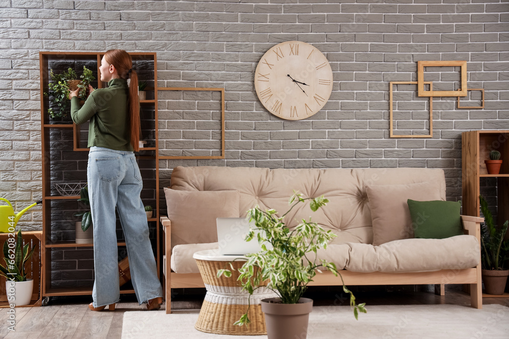 Young woman with plant on shelf at home, back view
