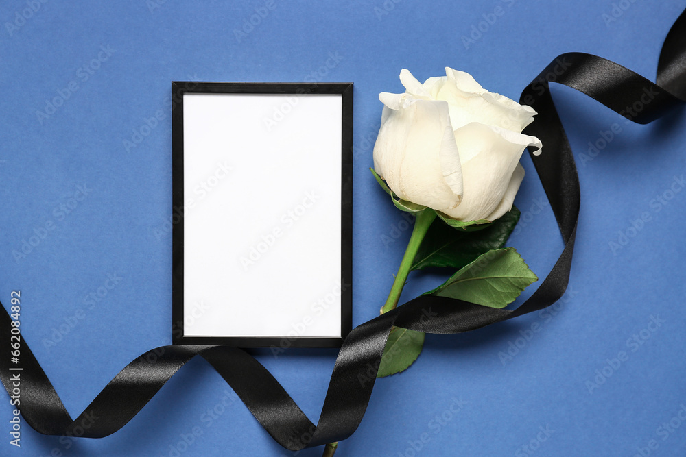 Black ribbon with photo frame and white rose on blue background