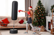 Sporty young woman with punching bag at home on Christmas eve