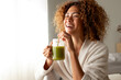 © Daniel - Happy multiracial woman enjoying healthy green juice at home. Female doing detox drinking green smoothie. Copy space.
