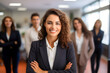 © Asiri - Leading with Confidence A Smiling, Attractive Professional Woman Strikes a Pose in Her Business Office, Surrounded by Her Coworkers and Employees in the Background