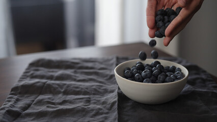 Wall Mural - man pour fresh blueberries into white bowl on table