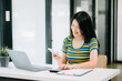© Nuttapong punna - Confident Asian woman with a smile standing holding notepad and tablet at the modern office..