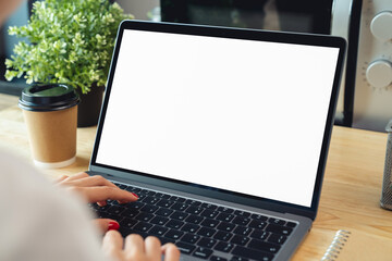 Woman hand using laptop and typing on keyboard with mockup of blank screen on wooden table.