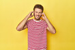 © Asier - Young Caucasian man on a yellow studio background covering ears with hands.