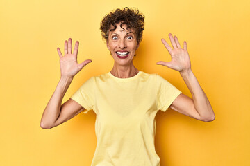 Wall Mural - Mid-aged caucasian woman on vibrant yellow showing number ten with hands.