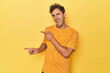 Young Latino man posing on yellow background pointing with forefingers to a copy space, expressing excitement and desire.