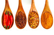 Vier braune Kochlöffel aus Holz mit unterschiedlichen Formen der Chili - die Peperoni darauf, weißer Hintergrund, horizontal