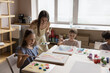 © fizkes - Group of cute little children engaged in painting class in art-studio, drawing pictures with paints on canvas, talking to painter teacher, enjoy creative hobby. Daycare, skill and talent development