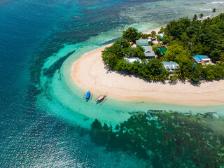 Shiny white sandy beach with two boats on turquoise water and corals. Beautiful waves around the island. San Victor Island. Mindanao, Philippines.