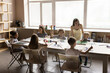 © fizkes - Group of little cute multiethnic children, boys and girls sit at table enjoy art classes in creative studio with young artist woman teacher. Day-care, talent and fine motor skills development, hobby