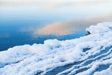 Wall Mural - Ice on the shore of lake. Sky with clouds reflected in the cold water at sunset.