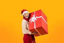 Woman In Santa Hat Holds Xmas Gift Over Yellow Backdrop