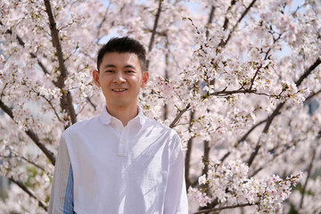 happy smile Asian young man and white sakura flower tree on sunny day
