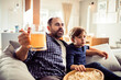 © Geber86 - Young Caucasian father watching sports with his son and cheering for their team on the couch in the living room at home