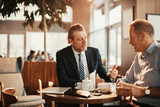 Fototapeta  - Two Caucasian middle aged businessmen having a meeting over some coffee in a café decorated for Christmas and the new year holidays