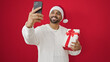 © Krakenimages.com - African american man taking a selfie picture holding christmas gift over isolated red background