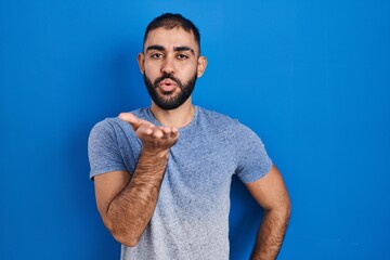 Canvas Print - Middle east man with beard standing over blue background looking at the camera blowing a kiss with hand on air being lovely and sexy. love expression.