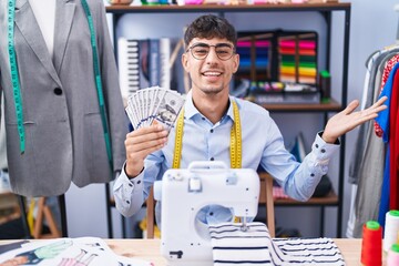 Young hispanic man dressmaker designer holding dollars celebrating achievement with happy smile and winner expression with raised hand