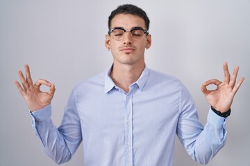 Wall Mural - Handsome hispanic man wearing business clothes and glasses relax and smiling with eyes closed doing meditation gesture with fingers. yoga concept.