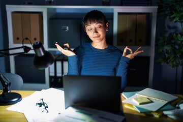 Wall Mural - Young beautiful woman working at the office at night relax and smiling with eyes closed doing meditation gesture with fingers. yoga concept.