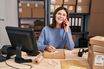 Canvas Print - Young blonde woman ecommerce business worker talking on smartphone writing on package at office