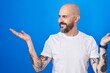 © Krakenimages.com - Hispanic man with tattoos standing over blue background smiling showing both hands open palms, presenting and advertising comparison and balance