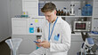 © Krakenimages.com - Handsome, serious-faced young caucasian male scientist engrossed in texting vital medical research on his smartphone in bustling lab workspace