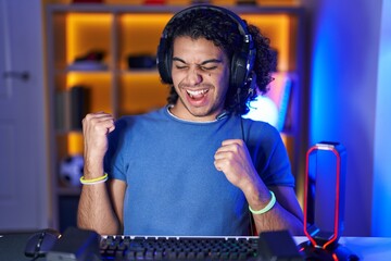 Poster - Hispanic man with curly hair playing video games celebrating surprised and amazed for success with arms raised and eyes closed