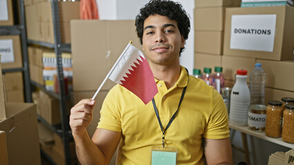 Sticker - Young latin man volunteer holding qatar flag smiling at charity center