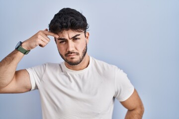 Sticker - Hispanic man with beard standing over white background pointing unhappy to pimple on forehead, ugly infection of blackhead. acne and skin problem