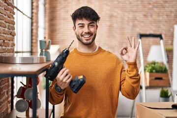 Wall Mural - Hispanic man with beard holding screwdriver at new home doing ok sign with fingers, smiling friendly gesturing excellent symbol