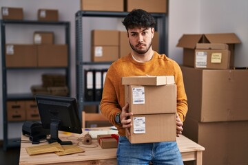 Sticker - Hispanic man with beard working at small business ecommerce holding packages skeptic and nervous, frowning upset because of problem. negative person.