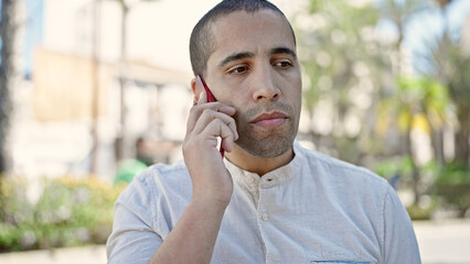 Wall Mural - Young hispanic man speaking on the phone looking serious at park