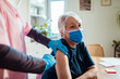 © Marko Geber - Senior woman getting vaccinated by her caregiver at home