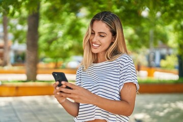 Wall Mural - Young blonde woman smiling confident using smartphone at park