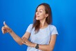 © Krakenimages.com - Brunette woman standing over blue background looking proud, smiling doing thumbs up gesture to the side