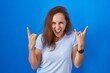 © Krakenimages.com - Brunette woman standing over blue background shouting with crazy expression doing rock symbol with hands up. music star. heavy music concept.