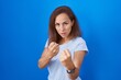 © Krakenimages.com - Brunette woman standing over blue background ready to fight with fist defense gesture, angry and upset face, afraid of problem