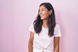 © Krakenimages.com - Young hispanic woman standing over pink background looking away to side with smile on face, natural expression. laughing confident.