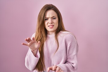 Wall Mural - Young caucasian woman standing over pink background disgusted expression, displeased and fearful doing disgust face because aversion reaction.