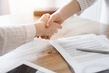 Business people shaking hands above contract papers just signed on the wooden table, close up. Lawyers at meeting. Teamwork, partnership, success concept