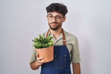 Canvas Print - Arab man with beard holding green plant pot winking looking at the camera with sexy expression, cheerful and happy face.