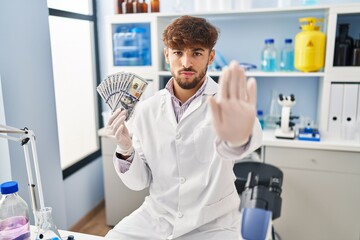 Canvas Print - Arab man with beard working at scientist laboratory holding money with open hand doing stop sign with serious and confident expression, defense gesture