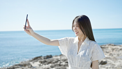 Poster - Young chinese woman smiling confident making selfie by the smartphone at seaside