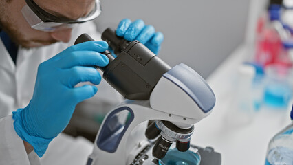 Wall Mural - Young hispanic man scientist using microscope at laboratory