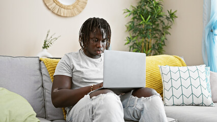 Sticker - African american man using laptop sitting on sofa at home