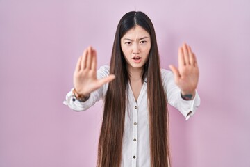 Wall Mural - Chinese young woman standing over pink background doing stop gesture with hands palms, angry and frustration expression