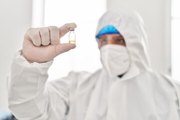 Canvas Print - Young latin man scientist wearing covid protection uniform holding vaccine dose at laboratory