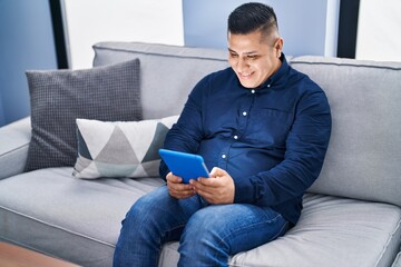 Wall Mural - Young latin man using touchpad sitting on sofa at home